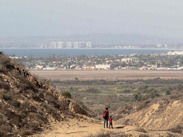 Migrante com o filho cruza a fronteira dos Estados Unidos a partir da cidade Mexicana de Tijuana. por GUILLERMO ARIAS/AFP