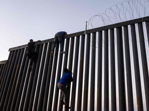 Migrantes escalam o muro da fronteira com os Estados Unidos em Playas de Tijuana, México. por GUILLERMO ARIAS/AFP