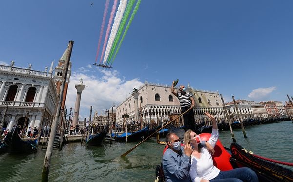 Em Veneza, na Itália, pessoas passeiam de gôndola e registram as acrobacias aéreas. por Andrea Pattaro/AFP