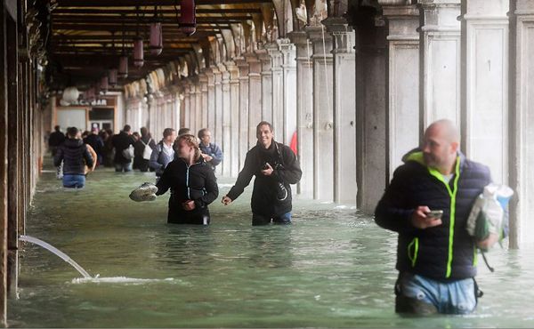 Turistas sob arcos inundados da Praça St Mark durante um período de alta-água (Acqua Alta) em Veneza. As inundações, causadas por uma convergência de marés altas e um forte vento Sirocco, atingiu cerca de 150 centímetros. por MIGUEL MEDINA / AFP