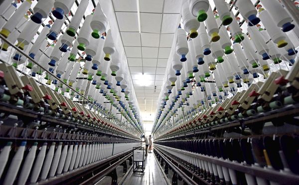 Trabalhadores em fábrica de tecidos na China. por AFP