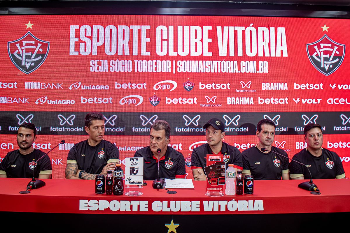 No centro da mesa da sala de imprensa da Toca do Leão, o presidente do Vitória, Fábio Mota, apresenta o novo técnico, Thiago Carpini