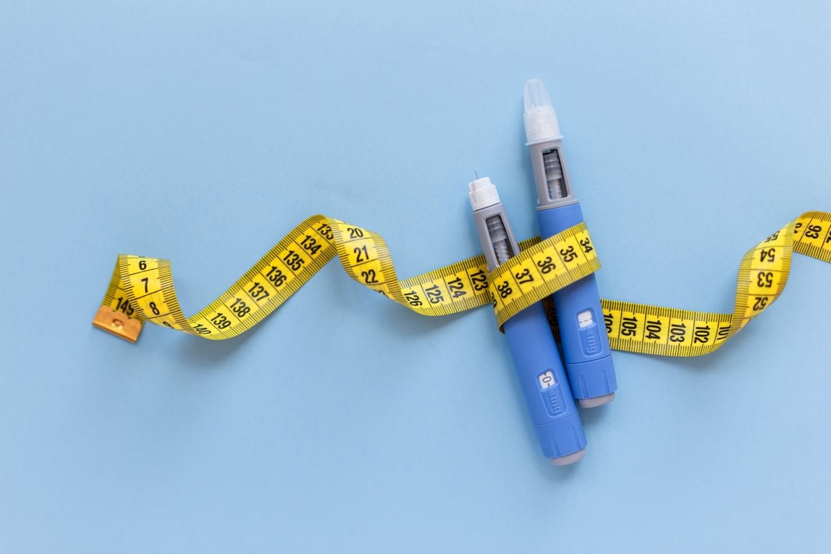 Two injectors dosing pens for subcutaneous injection of antidiabetic medication or anti-obesity medication hovering over a blue background. Yellow measuring tape around the injectors. antidiabetic