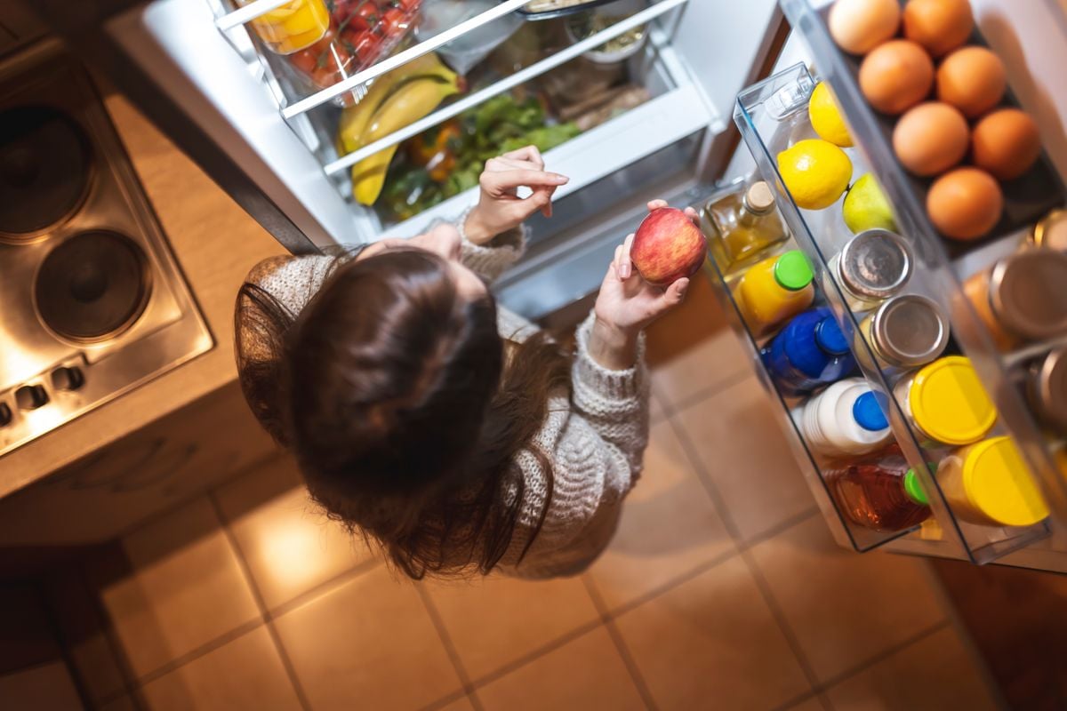 Mulher buscando comida na geladeira durante a noite