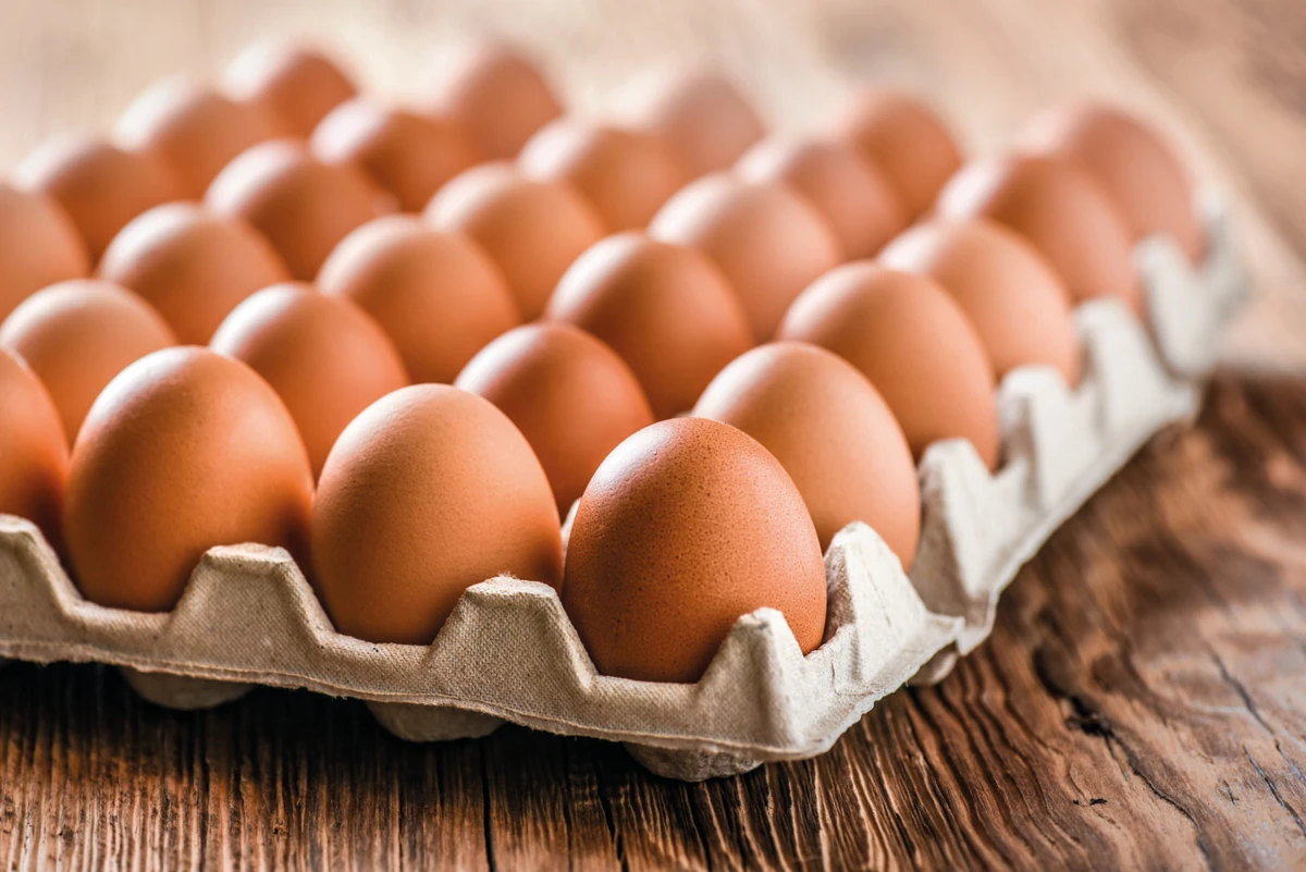 Chicken eggs in carton box on wooden table.  por Shutterstock