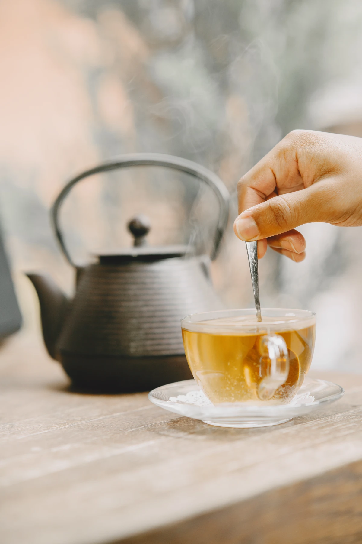 Teapot and cup of hot tea on a table. Hand holding a teaspoon. por Reprodução | Freepik