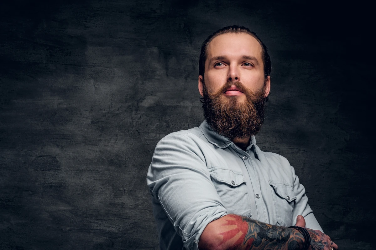 Groomed bearded man with tattooes is posing at dark photo studio. por Reprodução | Freepik