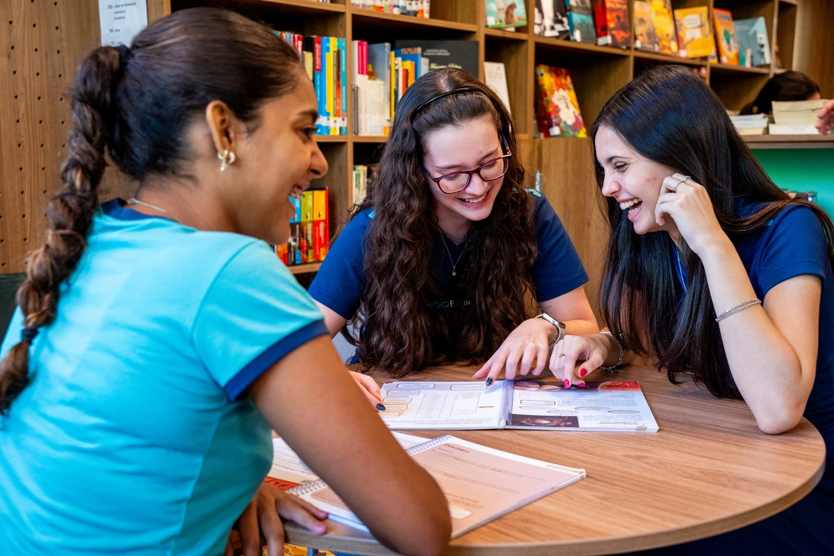 Alunas do Ensino Médio estudando juntas na biblioteca do Colégio Bernoulli, em ambiente de colaboração e troca.