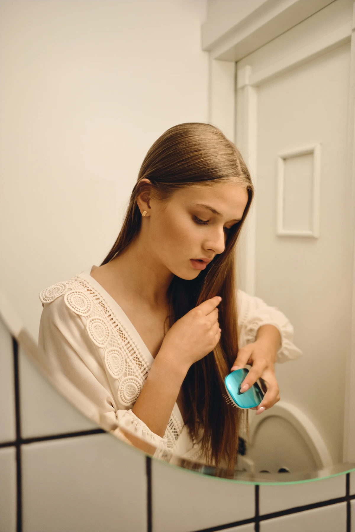 Young beautiful pensive woman in white dress standing near mirror dreamily brushing her hair in bathroom por Reprodução | Freepik