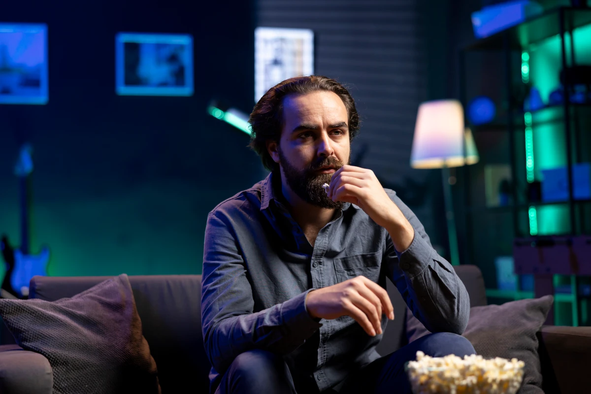 Puzzled man eating popcorn while watching confusing movie on streaming service, enjoying time off from work. Person consuming snacks, looking at films broadcasted on TV with convoluted plots por Reprodução | Freepik
